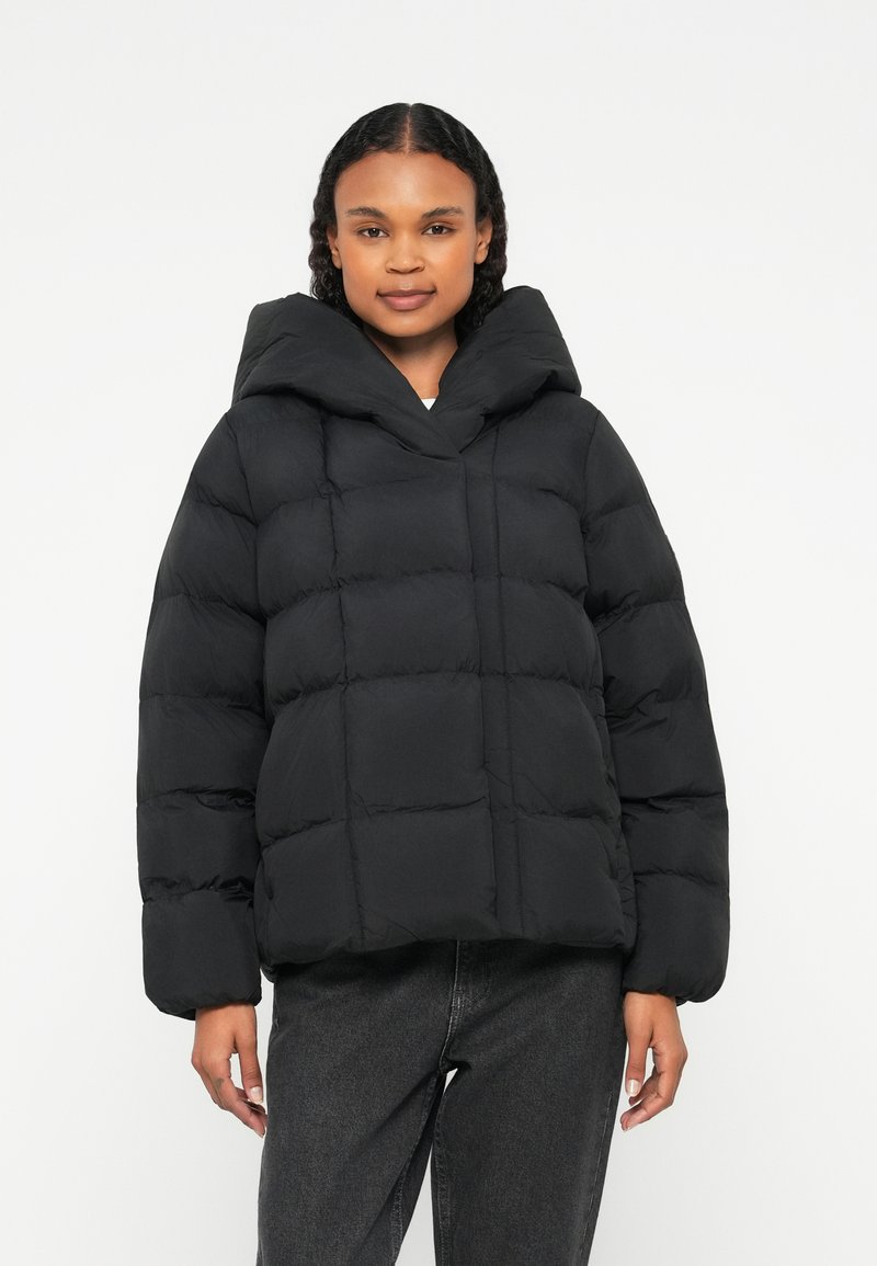 Čierna prešívaná bunda s veľkou kapucňou, prešívaným vzorom a voľným strihom. Má široké rukávy a minimalistický štýl.