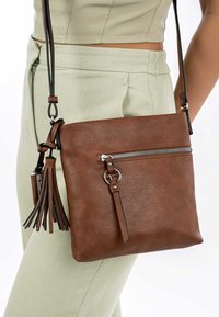 Hnědá kožená crossbody taška s kovovým zipem, přední kapsou a dekorativními třásněmi. Připojený nastavovací popruh.