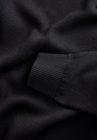 Primo piano di tessuto nero lavorato a maglia con dettaglio visibile del polsino a coste e pieghe morbide.