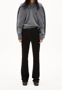 Šedý vlněný svetr vrstvený pod odpovídajícím oversized kardigánem, doplněný o černé zakázkové kalhoty. Texturovaný vzhled s knoflíkovými akcenty.