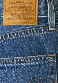 Levi's Denim-Jeans mit einem braunen Lederpatch mit geprägtem Logo. Blaue Stoffqualität mit orangefarbenen Nähten und genieteten Details.