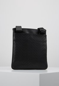 Černá kožená crossbody taška s herringbone vzorem, štíhlý obdélníkový tvar, nastavitelný popruh a texturovaný povrch.