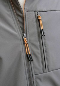 Grå jakke stof med orange lynlåse. Har et hybriddesign med kontrasterende sømme og en lynlåslomme. Holdbar og glat tekstur.