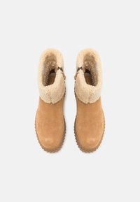 Botas de tobillo de ante color marrón claro con un puño de piel sintética color crema, presentan una cremallera lateral y una suela de goma texturizada para mayor tracción. Acabado suave en general.