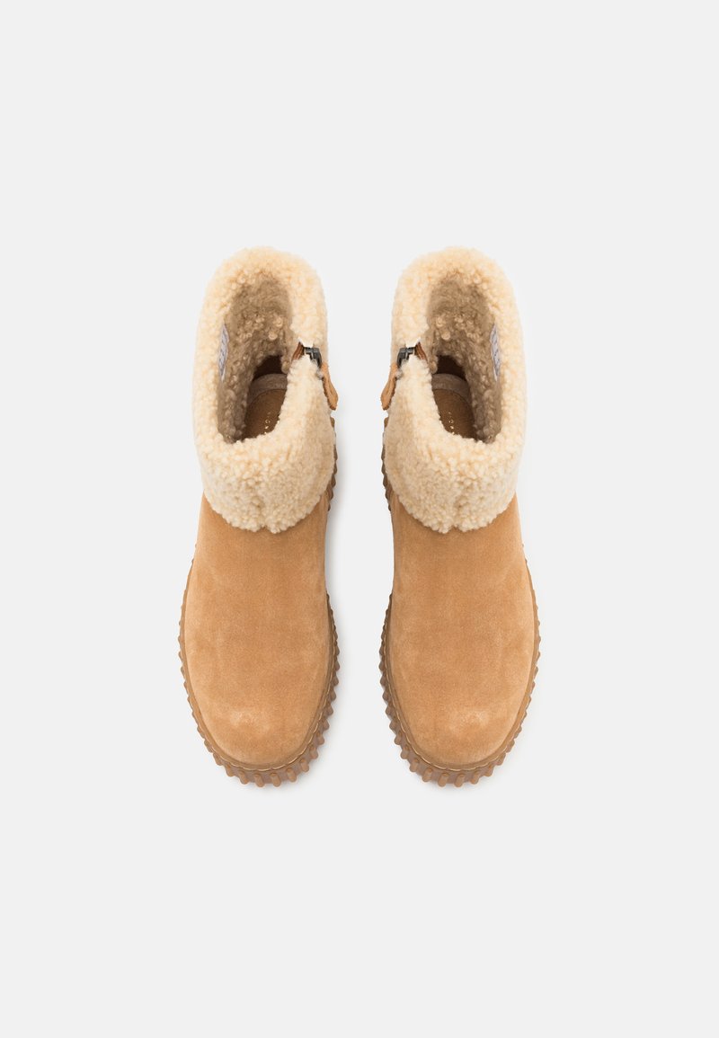 Bottines en suede beige avec un col en fausse fourrure crème, dotées d'une fermeture éclair sur le côté et d'une semelle en caoutchouc texturé pour une meilleure adhérence. Fini lisse dans l'ensemble.