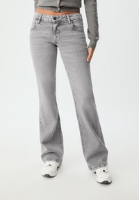 Grå utsvängda jeans med en urblekt finish, med knapp- och dragkedjestängning, framfickor och en avslappnad passform vid nederkanten.
