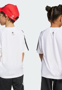 Białe koszulki sportowe z krótkim rękawem i czarnymi akcentami na rękawach, z logo Adidas i Marvel z tyłu, noszone przez dwoje dzieci.