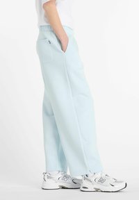 Un pantalon de survêtement bleu clair en matériau doux avec une coupe décontractée, des poches latérales et une taille côtelée, accompagné de baskets blanches et grises.