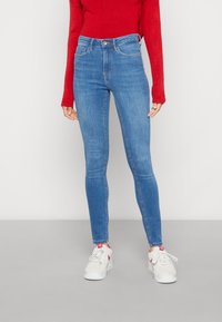 Vaqueros de mezclilla azul delgados con una cintura media, bolsillos frontales y un ligero desvanecimiento. Combinados con zapatillas blancas que tienen acentos en rosa.