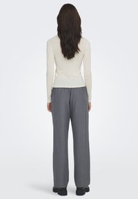 Top de manga larga color beige claro con textura acanalada, combinado con pantalones anchos gris con rayas finas, de corte relajado y costuras visibles. El conjunto se completa con calzado negro.