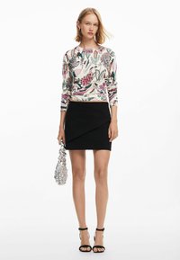 Maglione stampato con motivi floreali rosa e verdi, gonna nera aderente e borsa argentata; modella con tacchi neri a cinturino.