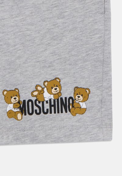 Az szürke pamut anyagon három mesei medve minta látható, akik fehér inget viselnek, alattuk pedig vastag fekete betűkkel olvasható a "Moschino" felirat.
