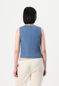 Denim brezrokavni top v svetlo modri barvi, s prilagojenim krojem, gladko teksturo in ravnim robom, nošen z svetlimi hlačami.