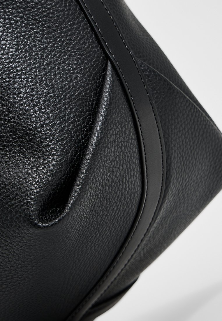 Schwarze Ledertasche mit strukturierter Oberfläche, die über geschwungene Designelemente und glatte Akzente verfügt. Enthält schwarze Nähte entlang der Kanten.