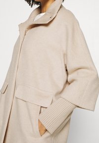 Beige wollen blend jas met een hoge kraag, geribde manchetten en twee voorkennis, met een ontspannen pasvorm en zachte textuur.