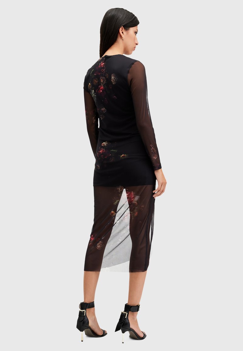 Vestido negro con mangas largas de malla transparente, superposición de patrón floral, longitud a media pantorrilla, diseño con abertura, combinado con sandalias de tacón alto negras.