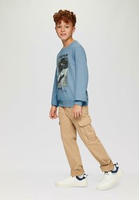 Lichtblauwe sweatshirt met lange mouwen en grafische print, gecombineerd met beige cargobroeken en witte sneakers met marineblauwe accenten.