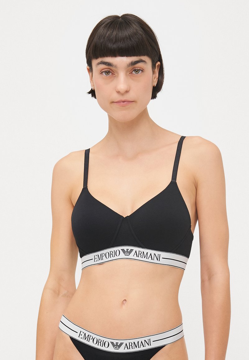 Black bra with adjustable straps, featuring a seamless design and a white logo band. The material appears smooth with slight stretch.