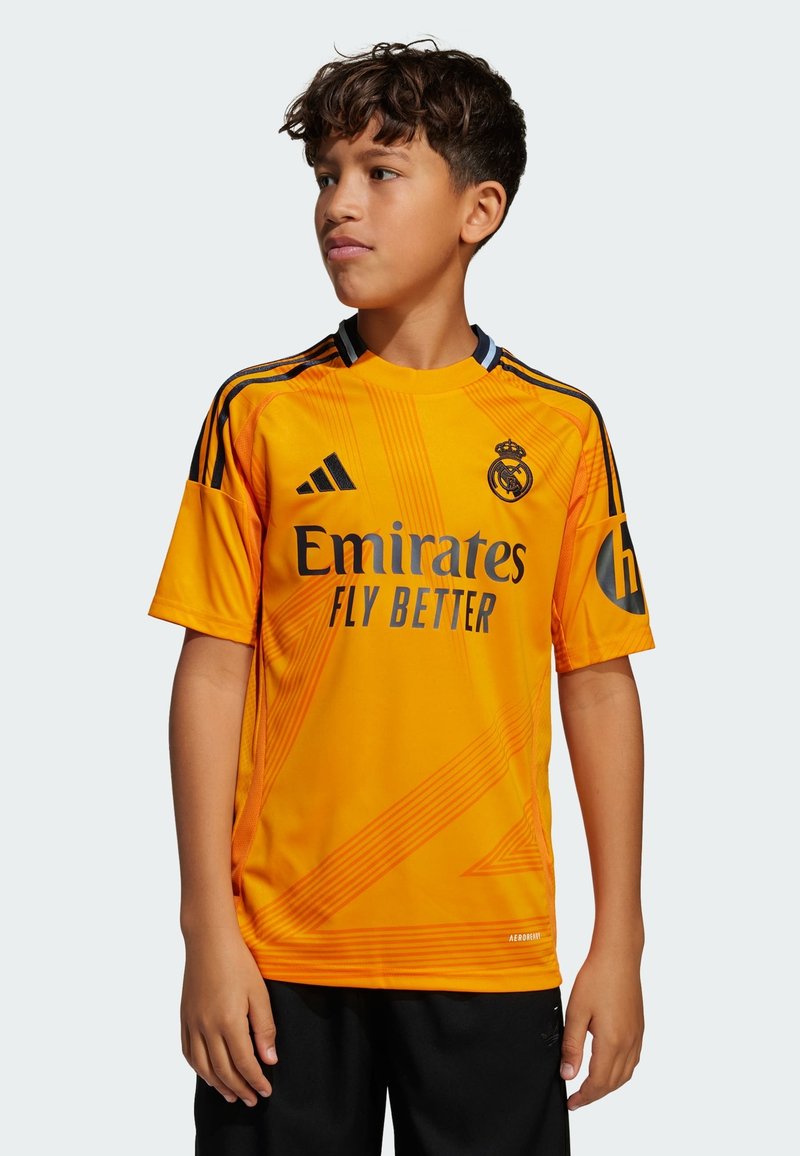Maillot de football orange à manches courtes, avec des accents noirs et le logo du Réal Madrid, portant le texte "Emirates Fly Better".