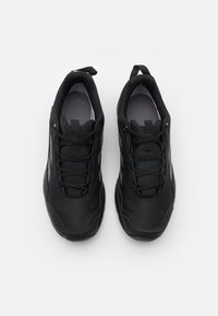 Schwarze Sportschuhe mit strukturiertem Obermaterial, ausgestattet mit Schnürsenkeln, einer Zuglasche und grauen Akzentstreifen an den Seiten. Ergonomisches Design und robuste Sohle.