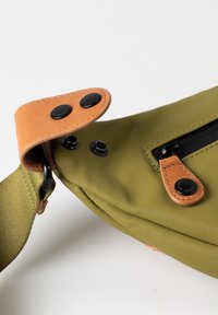 Groene stoffen schoudertas met leren accenten. Voorzien van een ritssluiting, drukknoopsluitingen en een gestructureerd oppervlak. Inclusief verstelbare schouderband.