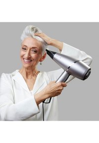 Ασημένιο πιστολάκι μαλλιών με ακίδα, εργονομική λαβή και μαύρες λεπτομέρειες; χρήστης με κοντά γκρίζα μαλλιά χτενίζει τα μαλλιά του.