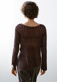 Pull en tricot de couleur violet foncé avec texture côtelée, col rond, manches longues et fentes latérales. Associé à un pantalon rayé.