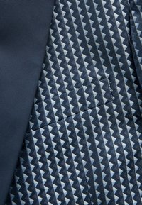 Granatowy materiał o żebrowanej fakturze po lewej, a z prawej strony geometryczny wzór w zygzaki w różnych odcieniach niebieskiego, z widocznym przeszyciem.