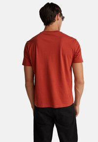 Camiseta roja de manga corta en tejido de algodón ligero, con cuello redondo y dobladillo recto, combinada con pantalones negros.