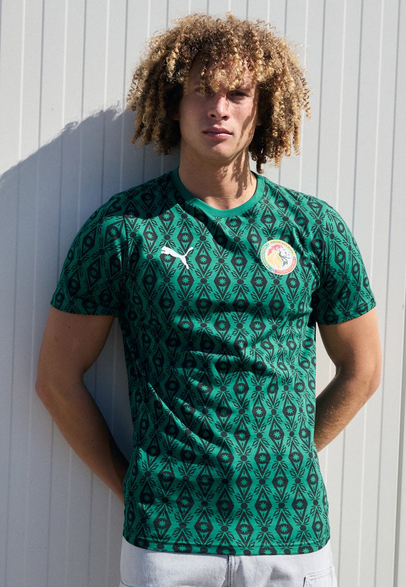 Grünes kurzärmliges Trikot mit filigranen schwarzen Diamant- und Blattmustern, ausgestattet mit einem runden Kragen und einem Logo auf der Vorderseite.