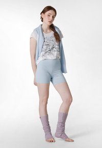 Ljusblå korta leggings i kombination med en vit t-shirt med text, och en mjuk ljusblå tröja draperad över axlarna. Lila benvärmare.