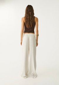 Débardeur marron associé à un pantalon large à jambe droite, fluide, à rayures verticales claires. Le tissu semble doux, léger et respirant.