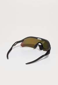 Occhiali da sole sportivi con montatura nera, forma curva e lenti con gradiente marrone. Grips testurizzati sul naso e stanghette eleganti e flessibili.