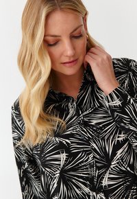 Blusa nera con bottoni caratterizzata da un motivo di foglie di palma in bianco, con una texture liscia e un design con colletto classico.