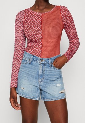 Långärmad bodysuit med två mönster: ett med röda blommotiver och ett med röda geometriska former. Kombineras med slitna denimshorts.