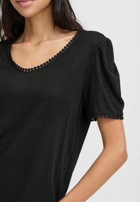 Juoda trumpa rankovė t-shirt su minkšta tekstūra, turinti vilktinį kaklo ir rankovių kraštus, bei laisvą siluetą.