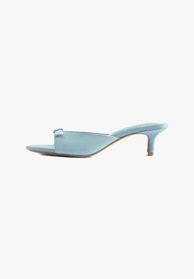 Mule en suède bleu clair à bout ouvert, à petit talon kitten et avec une petite boucle sur la bride supérieure.