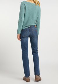 Tyrkysový svetr s texturovaným pletením, spárovaný s tmavě modrými džínami s rovnými nohavicemi. Hnědé kotníkové boty doplňují celý outfit.