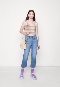 Top de croché com riscas rosa, verde e roxa, jeans de cintura alta azul claro, bolsa de palha beige e sapatos de plataforma roxos com meias combinando.