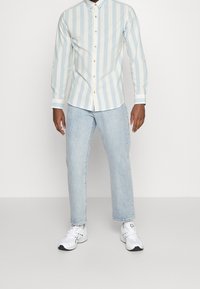 Camicia button-up a righe azzurre e bianche, maniche lunghe con polsini bianchi, abbinata a jeans dritti azzurri e sneakers bianche.