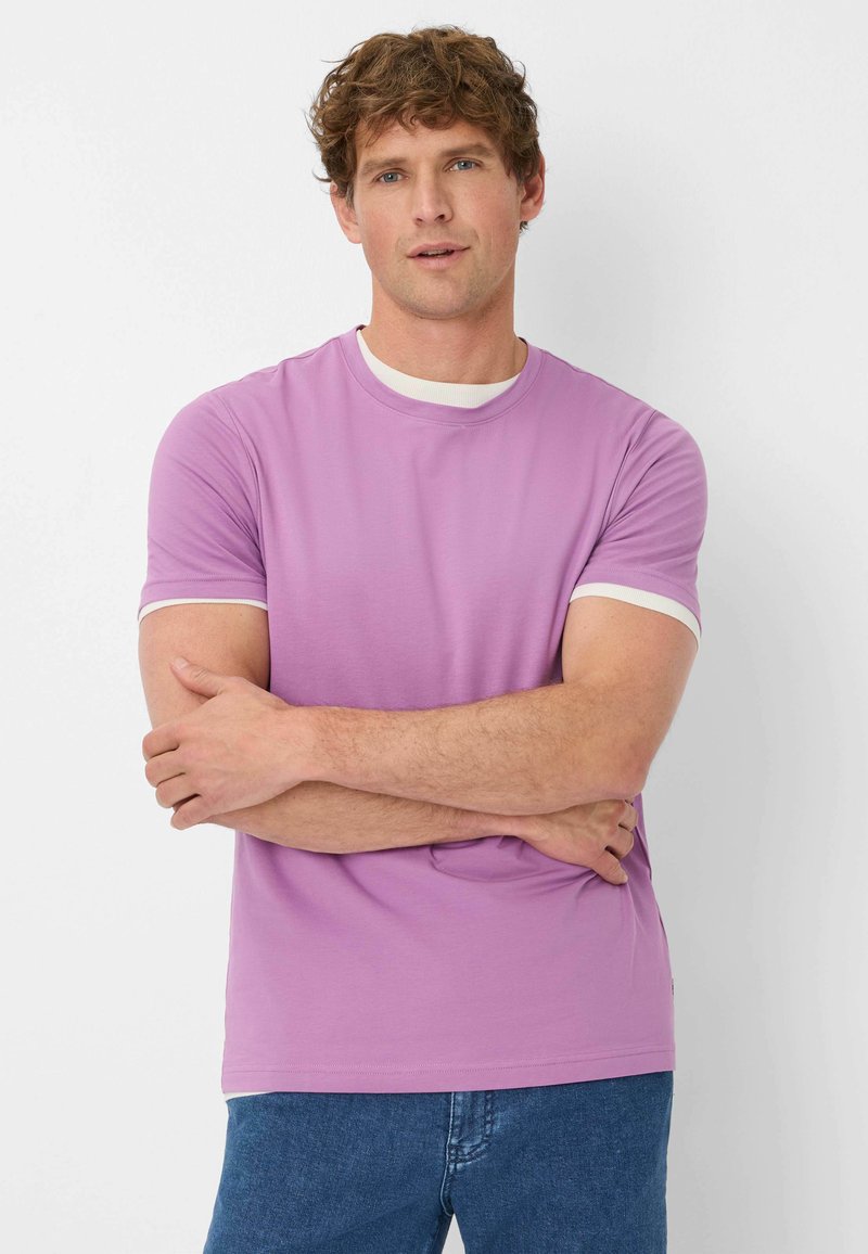 T-shirt viola chiaro con collo rotondo e bordo bianco, maniche corte, realizzata in tessuto morbido. Indossata con jeans in denim blu.
