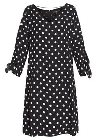 Vestido negro con lunares blancos, escote en V, mangas tres cuartos con detalle de lazo, tela ligera, hasta la rodilla, corte relajado.