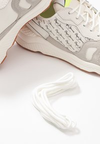 Białe i szare sneakersy z brandingiem "Pepe Jeans London" oraz skręconą parą białych sznurowadeł na białym tle.