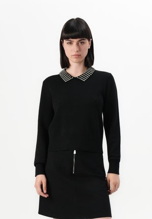 Black sweater with a contrasting embellished collar, ribbed cuffs and hem, worn with a matching black skirt featuring a zip detail.