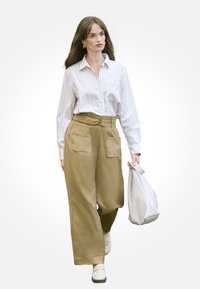 Beżowe spodnie o szerokich nogawkach z bocznymi kieszeniami, zestawione z białą koszulą na guziki w poziome paski oraz jasną torbą.