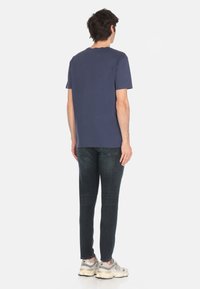 T-shirt in cotone blu navy con collo rotondo e maniche corte, abbinata a jeans in denim scuro slim-fit e sneakers atletiche grigio chiaro.