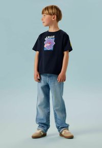 Marineblå T-skjorte med et Gengar-motiv, kombinert med lyseblå jeans og beige joggesko. T-skjorten har korte ermer og en avslappet passform.