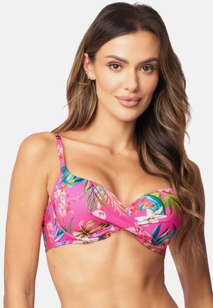 Roze bikinitop met een bloemenpatroon met groene bladeren en witte orchideeën. Heeft verstelbare schouderbanden en een gedraaide voorkant.