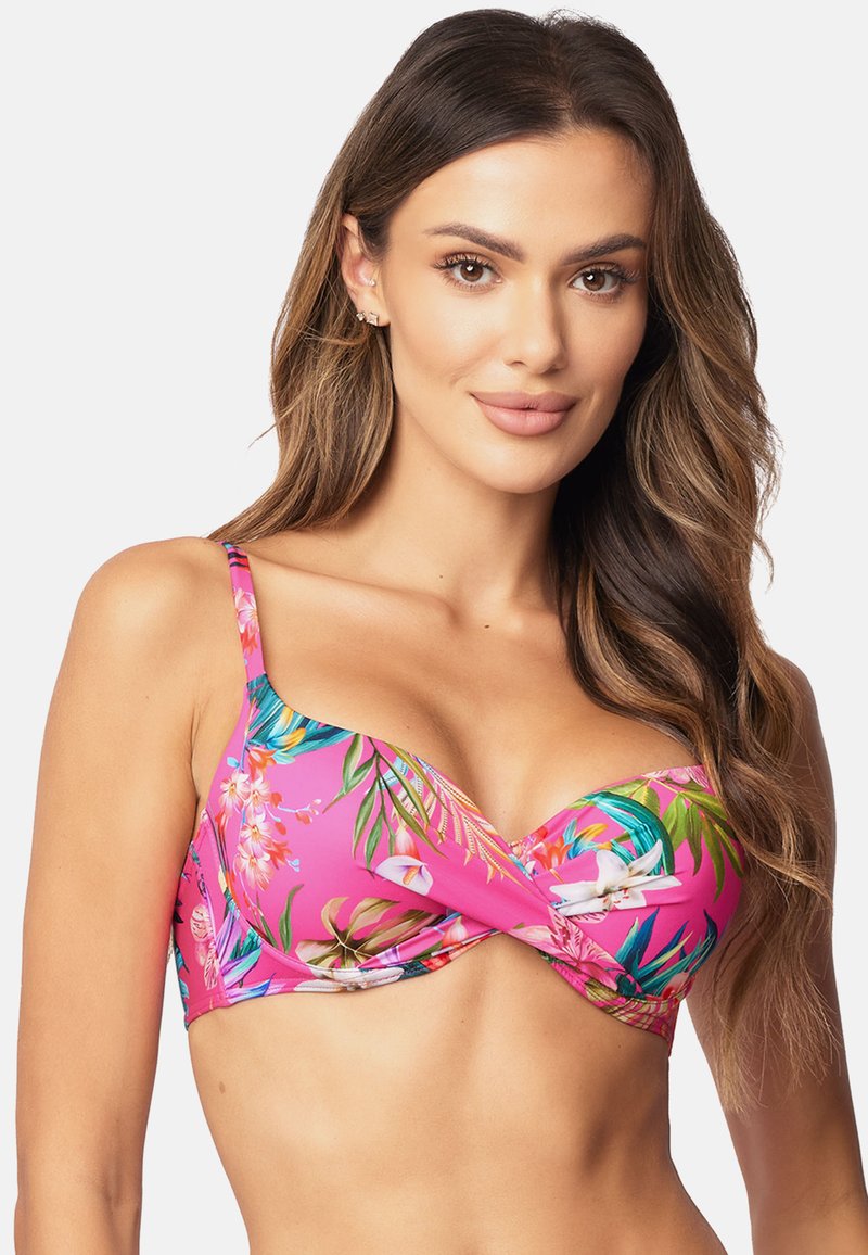 Roze bikinitop met een bloemenpatroon met groene bladeren en witte orchideeën. Heeft verstelbare schouderbanden en een gedraaide voorkant.