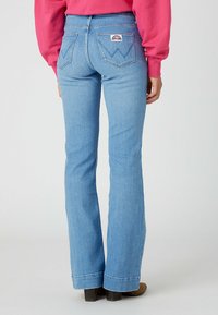 Jeans a campana di colore blu chiaro con un classico design a cinque tasche, che mostrano una forma distintiva della tasca posteriore e un'etichetta di marca sulla cintura.